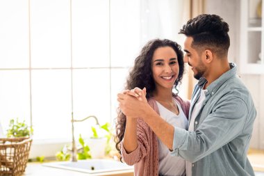 Romantik anlar. Orta Doğulu mutlu eşlerin mutfakta dans edip gülümsemesi, modern Arap ailesinin evde eğlenmesi, genç çiftin el ele tutuşması ve kaynaşması, kopyalama alanı.