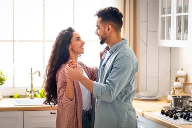 Mutfakta birbirine bağlanan mutlu Arap eşlerinin portresi, Orta Doğulu erkek ve kadını seven, el ele tutuşan ve birbirlerine gülümseyen, evde romantik anlar yaşayan, özgür kalan