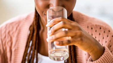 Ferahlatıcı içecek. Güzel siyah bayan, evde bardaktan su içiyor, mutfakta dinlenirken temiz mineral sıvısının tadını çıkarıyor, vücut suyu için sağlıklı bir içecek alıyor, kapatılıyor,