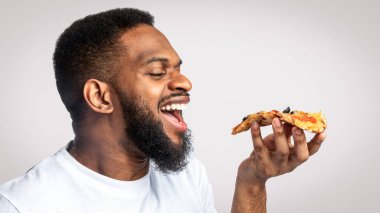 Beyaz stüdyonun arka planında pizza yiyen Afrikalı adamın yan görüntüsü. Abur cubur yiyenler portresi. Sağlıksız beslenme ve aşırı yeme alışkanlığı. Pizza Teslimatı