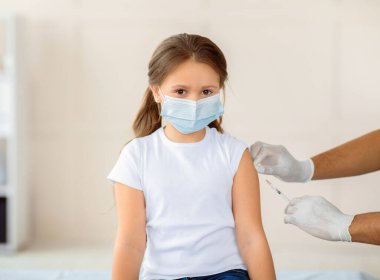 Yüzü maskeli küçük bir kız hastanede kovid 19 'a karşı aşı oluyor. Sağlık merkezinde koronavirüs aşısı olan sevimli bir çocuk. Bulaşıcı hastalıklara karşı koruma