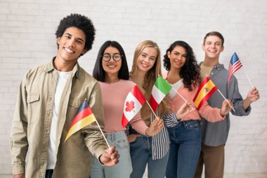 Uluslararası öğrencilerin ya da göçmenlerin modern eğitimi. Mutlu nesil z çok ırklı insanlar farklı ülkelerde bayraklar sallıyor üniversite sınıfında beyaz duvar arkasında, stüdyo çekimlerinde, boş alanlarda