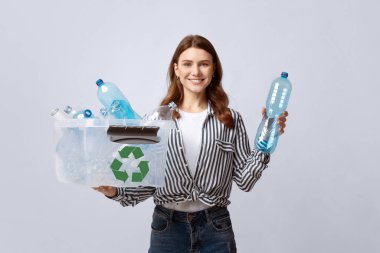 Atık ayıklama. Gülümseyen Eko Gönüllü Kadın Boş Plastik Şişelerle Konteynır Tutuyor, Neşeli Kadın Çöp Geri Dönüşümü Konseptini Desteklerken Gri Stüdyo Arkaplanı Üzerinde Poz Veriyor, Boş Alan