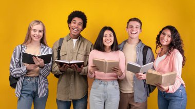 Modern ve işbirlikçi öğrenme, bilgi paylaşımı, mutluluk grubu. Gülümseyen çok ırklı genç öğrenciler kitap ve notlar okuyor, turuncu arka planda izole edilmiş, fotokopi alanı, stüdyo çekimi