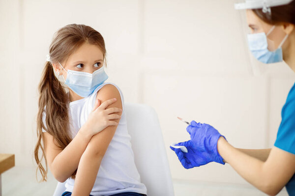 Маленькая девочка в маске для лица боится коронавирусной вакцины, не позволяя доктору делать инъекции в клинике. Ребенок боится вакцинации против ковида-19. Иммунизация против глобальной концепции вируса