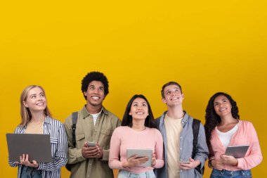 Öğrenciler için harika bir teklif, önemli bilgiler ve reklam. Sırt çantalı gülümseyen genç uluslararası insanlar, cihazlar yukarı bakıyor, turuncu arka planda izole edilmiş, stüdyo çekimi, boş alan, kare