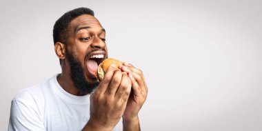 Aç Afrikalı Adam Açgözlülükle Burger yiyor Sağlıksız Fast food yiyor Beyaz Stüdyo Arkaplanı 'nın başında dikiliyor, Diyet Günü' nde Aldatıyor. Abur cubur ve aşırı yeme sorunu kavramı
