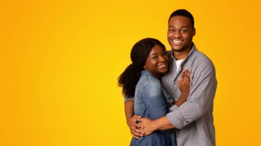 Sarı arka planda poz verirken birbirini seven siyah çiftin portresi, romantik bin yıllık Afro-Amerikan erkek ve kadın kameraya sarılıp gülümsüyor, mutlu duygular ifade ediyor, boşluğu kopyalıyor.