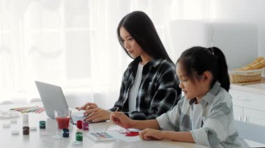 Samimi bir mutfakta, bir anne dizüstü bilgisayarıyla çalışırken kızı resim yapar, yaratıcılık ve beraberlik yoluyla sıcak bir ev ortamında aralarındaki bağı gösterir..