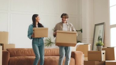 Genç bir çift yeni dairelerinde kutuları taşırken gülümsüyor. Paketlenmiş kutular ve ışıkla dolu rahat bir yaşam alanı ile çevrili yerlerinin değiştirilmesi konusunda heyecanlılar..