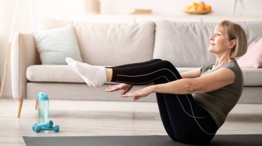 Son sınıf atletik kadın karın kasları egzersizi yapıyor, evde yoga pozisyonu alıyor, boş yer var. Koronavirüs salgını sırasında aile eğitimi alan sağlıklı bir kadının uzun bir portresi.