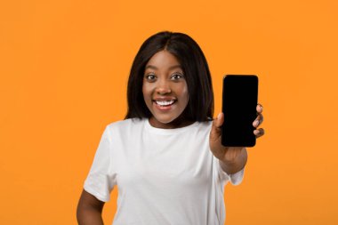 Uygulama ekranı ya da metin için bir model. Akıllı telefon, neşeli siyah kadın eli ile boş ekran, turuncu stüdyo arka planı, yakın çekim. Boş cep telefonu ekranı gösteren Afro-Amerikan güzel kadın.