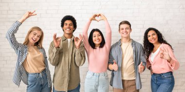 Aşk, arkadaşlık, gençlik, yaşam tarzı. Elleriyle hareket eden mutlu gençler, sıradan insanlar, beyaz tuğlalı arka planda, panoramada, kopyalama alanında kameraya bakıp eğleniyorlar.