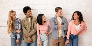 İlginç bir teklif ve takım, kolejde ya da üniversitede grupla eğitim ve öğrenim. Gülümseyen çok ırklı gençler beyaz duvar arkasında, stüdyo çekimlerinde, boş alanda İspanyol bayan arkadaşa bakıyorlar.