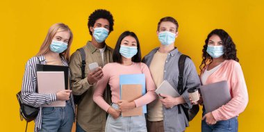 Yurtdışında eğitim ve öğrenci değişim programları. Modern neşeli gençler not defterleri, cihazları, kahve fincanları ile turuncu arka planda izole edilmiş kameraya bakan çok ırklı öğrenciler.