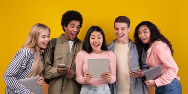 Modern cihazlar, sosyal ağlar ve eğitim. Şok olmuş genç çoklu etnik öğrenciler dijital tabletle Asyalı kadınların ellerinde, ağızları açık, turuncu arka planda izole edilmiş, kopyalama alanı