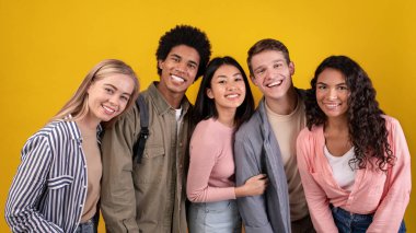 Göçmenlik ve yurtdışında eğitim, modern öğrenim ve takım çalışması. Mutlu genç çok ırklı öğrenciler eğleniyor, sarılıyor ve kameraya bakıyor, turuncu arka planda izole edilmiş, fotokopi alanı, stüdyo çekimi