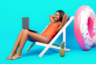 Dinlenmiş siyahi bir kadın dizüstü bilgisayarla şezlongda dinleniyor. İnternetten tropik cennetten iletişim kuruyor. Yaz tatilinde iyi bir film izliyor. Boşluğu kopyala