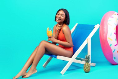 Uzunluğu, şezlongda tropikal kokteyl içen, mayo giyen ve mavi arka planda kahkahalar atan, boş alan olan bir kadın. Yaz tatili boyunca plajda takılan genç bayan.