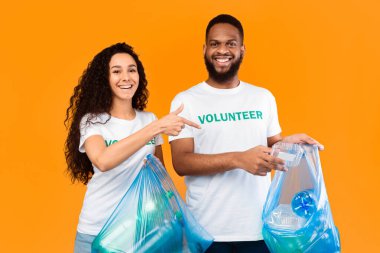 Çamur atma. Erkek ve Kadın Çoklu Kültürlü Gönüllüler Atık Plastik Temizlik ve Çöp Toplama Bölümü Sarı Stüdyo Arkaplanı Üzerinde Mavi Çöp Torbaları Poz Veriyor. Ekoloji, Çevreyi Temiz Tut