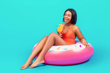 Modaya uygun mayo giyen, şişme ringde oturan, mavi arka planda meyve kokteyli içen, fotokopi çeken genç siyahi bir bayan. Havuzlu seksi kadın yüzer ve serinletici bir içecek hazırlar plaj partisine