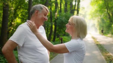 60 'lı yaşlarda bir çift yemyeşil bir parkta birlikte koşmaktan ve aktif yaşam tarzlarını göstermekten zevk alıyor. Gülümsemeleri ve kahkahaları paylaşıyorlar, doğada fitness ve arkadaşlığı kucaklıyorlar..