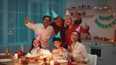 Aile üyeleri doğum gününü kutlamak için bir şenlik masasının etrafında toplanıyor, parti şapkaları takıyor ve gülümsemelerini paylaşıyorlar. Atmosfer kahkahalarla, güzel yemeklerle ve keyifli anlarla dolu..