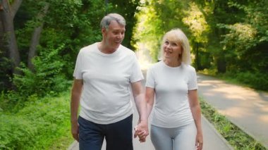 60 'lı yaşlarda üst düzey bir çift yemyeşil bir parkta el ele yürürler. Sağlıklı ve aktif bir yaşam tarzı sergilerler..