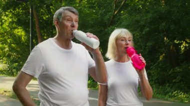 60 'lı yaşlarda bir çift canlı şişelerinden su içerek yemyeşil bir parkta koşuyor. Yeşilliğin ortasında, açık havada sağlık ve mutluluk gösteren aktif bir yaşam tarzını benimsiyorlar..