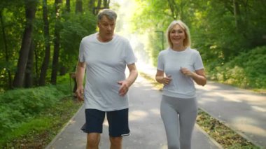 Yaşlı bir çift yeşil bir parkta yan yana koşuyor, açık havanın tadını çıkarıyorlar. Rahatlık için giyinmişler ve bu güzel ortamda egzersiz yaparken mutlu görünüyorlar..