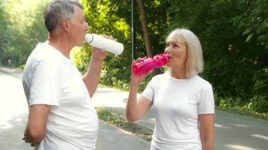60 'lı yaşlarda yaşlı bir çift, huzurlu bir parkta koşuya ara verip renkli şişelerden su yudumlarken aynı zamanda açık havada eğleniyor ve birbirlerine eşlik ediyorlar..
