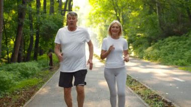 60 'lı yaşlarda bir çift yemyeşil ile çevrili bir parkta mutlu bir şekilde koşuyor. Aktif bir yaşam tarzını benimserler, açık havadan zevk alırlar ve egzersiz yaparken birbirlerine eşlik ederler..