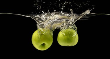 Hava kabarcıklarıyla suya batan iki yeşil elma, siyah arkaplan