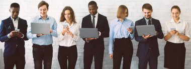 Dizüstü bilgisayarlar, tabletler ve akıllı telefonlar kullanan çok kültürlü iş adamları sırada bekliyor.