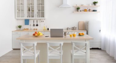 Sabahları rahat mutfak, çağdaş tasarım. Elmalı, fincanlı, dizüstü bilgisayarlı ve telefonlu, bardaklı ve sürahi portakal suyu masada, beyaz sandalyeli, mobilyalı, çatal bıçaklı, aydınlık duvarlı, perdeli