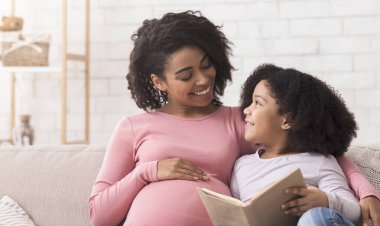 Güzel siyah kız ve hamile annesinin birlikte kitap okumaktan zevk aldığı, kanepede oturup gülümsediği, panorama