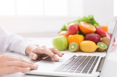 Doktor diyetisyeninin iş yerindeki dizüstü bilgisayarında taze meyve ve boş alanla daktilo etmesi.