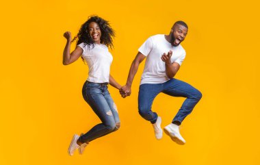 Neşeli siyah çift sarı arka plan üzerinde eğlenmek, havada atlama, adam kamera işaret