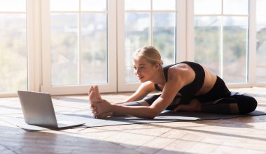 Spor başvurusu, web sitesi. Esnek genç kadın evde yoga yapıyor, dizüstü bilgisayar kullanıyor, kopyalama alanı kullanıyor.