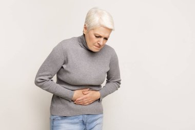 Mutsuz, yaşlı bir kadın midesini tutuyor. Gıda zehirlenmesi yüzünden karın ağrısı çekiyor. Boşluğu kopyala