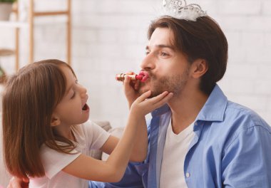 Evde ruj süren küçük bir kız, baba tacı takıyor, kopyalama alanı kullanıyor.