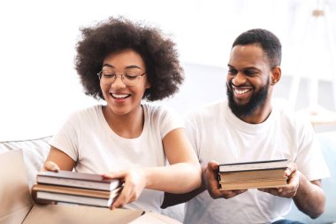 Neşeli siyah çift taşınma kutularını kapalı bir yere koyuyor, kitapları karton kutuya koyup yeni eve taşınmaya hazırlanıyor. Aile Konutları, Gayrimenkul Satın Alma Konsepti