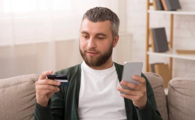 Online ödeme. Orta yaşlı adam kredi kartı tutan ve internet, ev iç, kopya alanı alışveriş için cep telefonu kullanarak