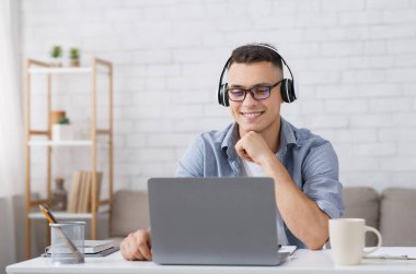 Ders ver, giyin ve Covid sırasında sınıfla birlikte çalış. Kulaklıklı ve gözlüklü gülümseyen çocuk dizüstü bilgisayara bakıyor. İnternette, oturma odasının içinde kendini izole etme hakkında ders veriyor.