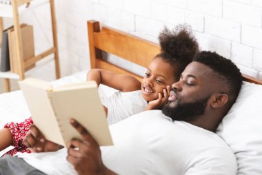 Sevgili Afrikalı baba küçük kızına masal okuyor, evde yatakta yatıyor.