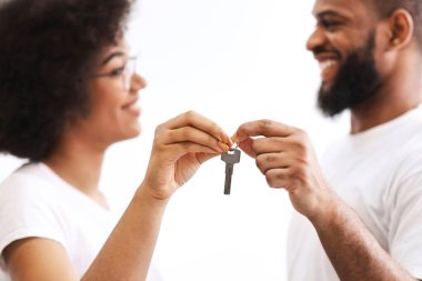 Neşe dolu siyah çift yeni evin anahtarını tutuyor. Birbirlerine gülümsüyor, beyaz arka planda poz veriyor, anahtarlara odaklanıyor. Apartman mülkiyeti, gayrimenkul ve aile konutları