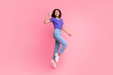 Mutluluk Konsepti. Genç Asyalı enerjik bir kadının tam boy portresi atlıyor ve pembe stüdyo arka planında iki parmak izole edilmiş zafer işareti işareti gösteriyor. Heyecanlı kadın zaferi kutluyor