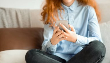 Dijital Yerliler, İç Güvenlik Üretimi. Tanımlanamayan, gülümseyen, akıllı telefon kullanan, internetten video izleyen, evdeki kanepede ya da yatak odasında bacak bacak bacak üstüne atmış bir çocuğun yakın çekimi.