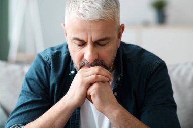 Düşünceli yaşlı sakallı bir adam evdeki oturma odasında kanepede oturuyor, ellerine yaslanıyor ve aşağı bakıyor, finansal sorunları var ya da bir şeyler düşünüyor, yakın plan, kopyalama alanı.