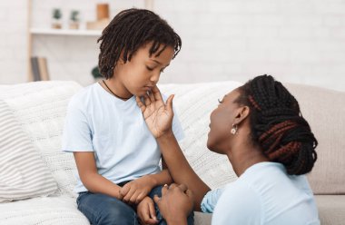 Teselli ve bakım. Afro anne üzgün kızını destekliyor, özür diliyor, gücenmiş çocuğunu okşuyor.
